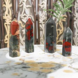 HerMJ Bloodstone Towers On Table - Red and black gemstone healing crystals, polished obelisk points, on a marble table with decorative background, showcasing unique mineral patterns and vibrant colors, ideal for jewelry, decor, and spiritual healing.