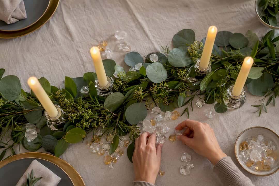 Decorazioni natalizie per la tavola con cristalli e pietre preziose in 10-30 minuti con HerMJ Mani che sistemano pietre e candele sul verde